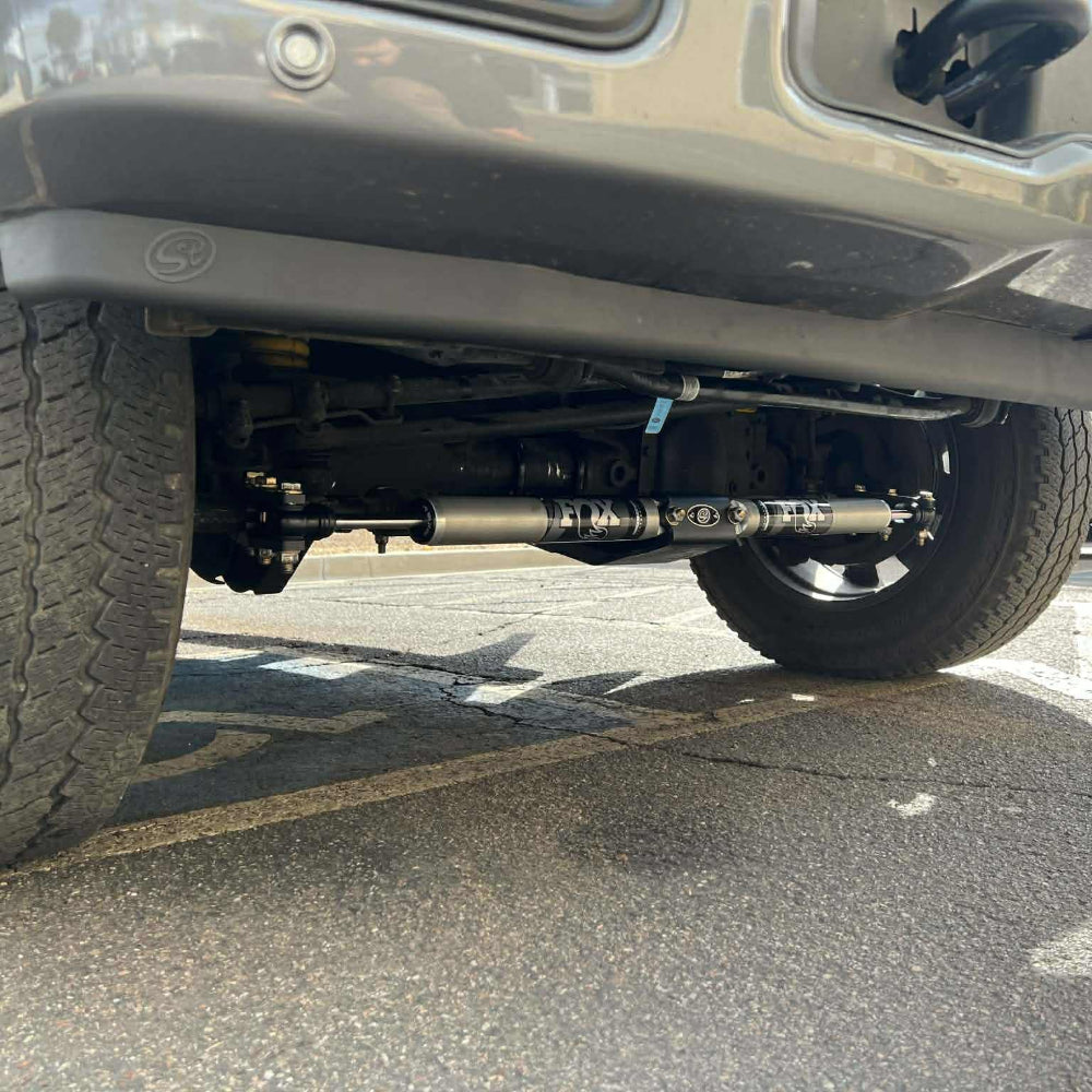 Close-up of a vehicle's undercarriage with suspension components on a paved surface.