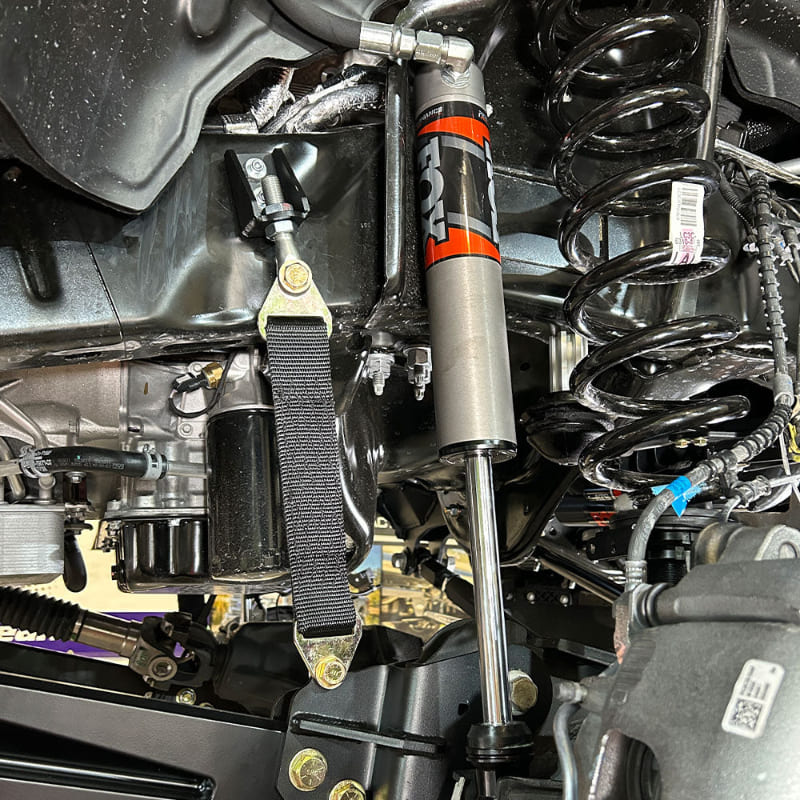 A black limit strap kit installed on a vehicle, showing the strap attached to the frame underneath the car.