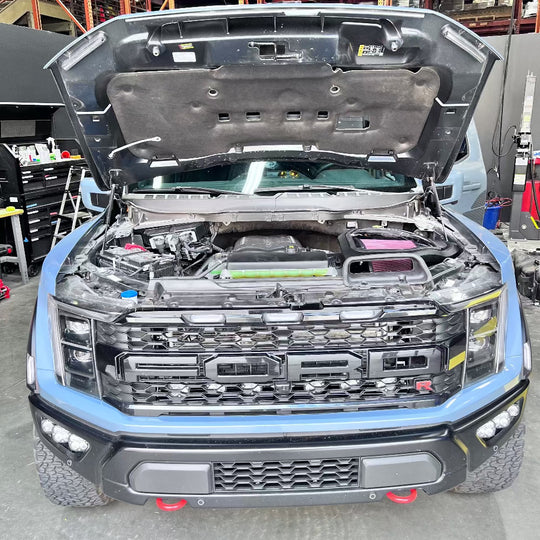 
  Blue truck with open hood in a workshop setting with an Cold Air Intake for the 2023-2025 Ford F-150 Raptor R with 3.8L Whipple Supercharger installed in the engine compartment of a vehicle
