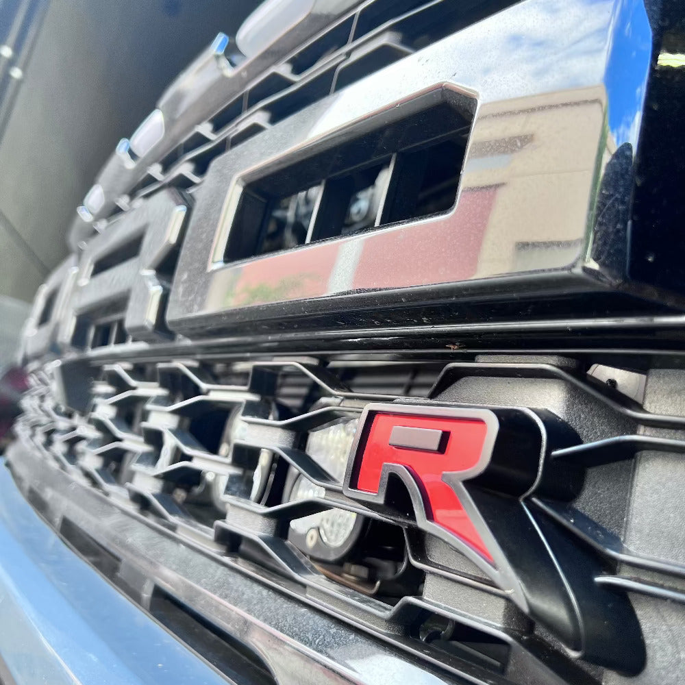 Close-up of a car grille with an Blue truck with open hood in a workshop setting with an Cold Air Intake for the 2023-2025 Ford F-150 Raptor R with 3.8L Whipple Supercharger installed in the engine compartment of a vehicle