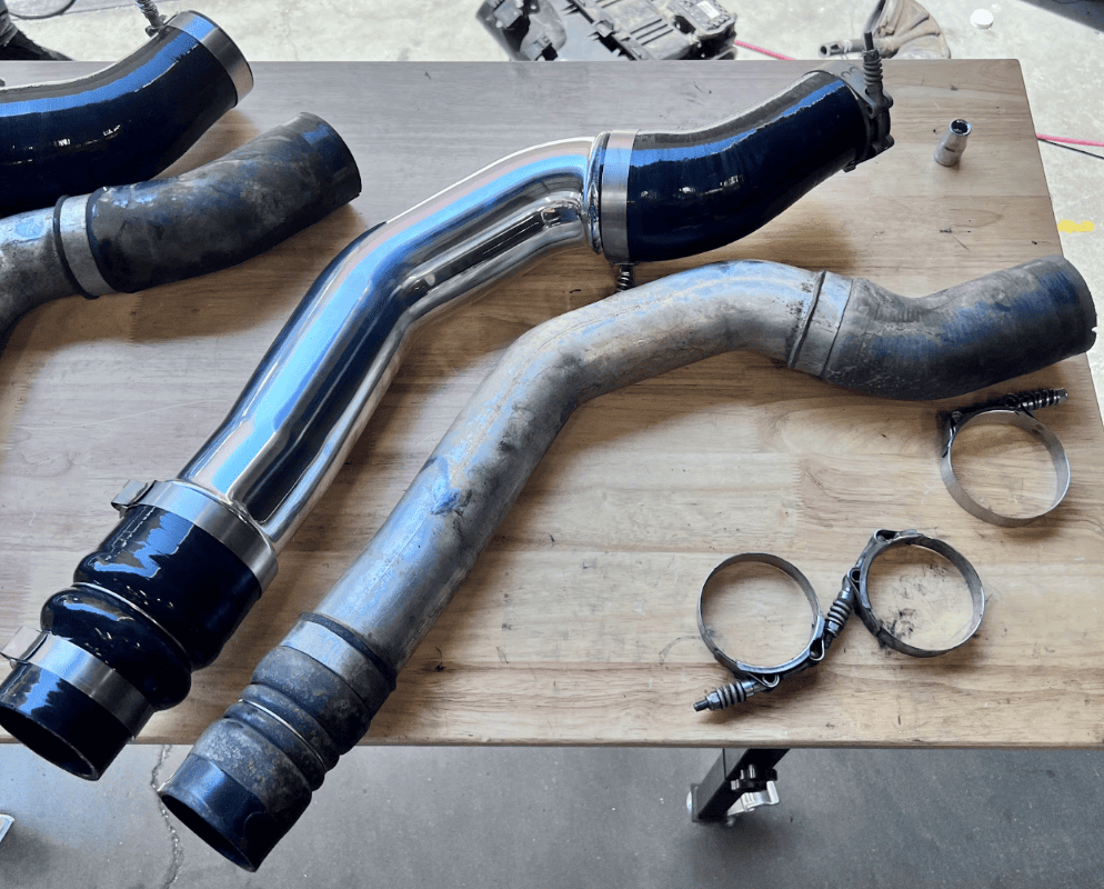 Comparisons between an old intercooler and new S&B Intercooler Pipe and Boot Set, 2013-2018 Ram 2500/3500 Cummins 6.7L and being held by a person in a garage setting.