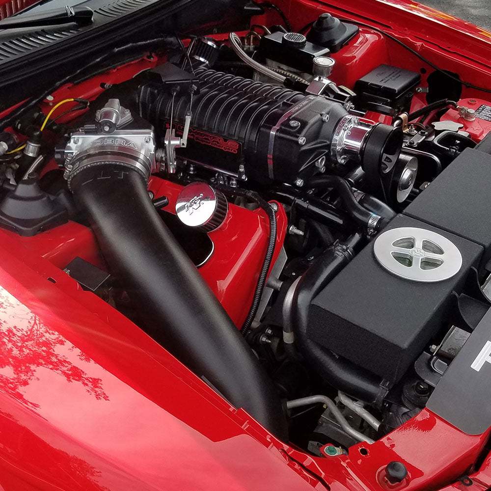 A JLT 12" High Boost Cold Air Intake for 2003-2004 SVT Cobra installed in the engine compartment of a red vehicle.