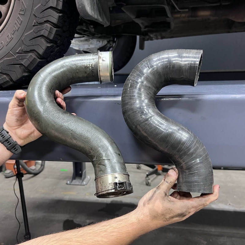 Two metal SB Filters Cold Side Intercooler Pipe for 2019-2022 Mercedes Sprinter 3.0L Diesel  held by a person with a vehicle in the background