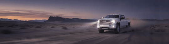
  White truck driving on a desert road with a sunset sky
